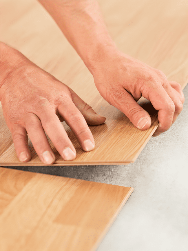 Hands installing wooden laminate flooring.