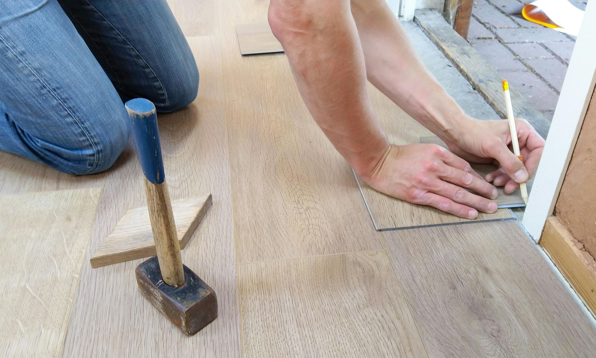 Person measuring laminate flooring with pencil.