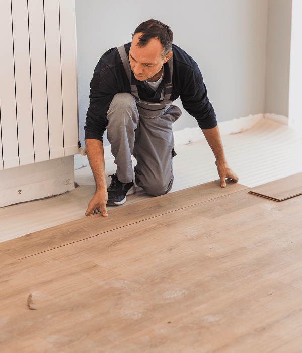 Man installing wooden flooring in room.